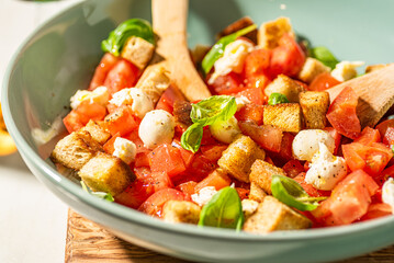 Classic italian panzanell salad with tomatoes, basil, bread, mozzarella on white kitchen table. Served with wine. Overhead view.