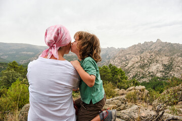 A Woman with cancer relaxing in nature. She is with her son who is giving her a kiss.