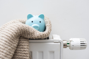Piggy bank with scarf on radiator. Concept of heating season.