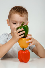 Fototapeta premium Surprised excited 7s boy, posing fresh peppercorn, looking at camera isolated on white background, studio portrait. Little boy sitting with three paprika of red, green, yellow colors.