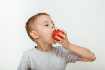 The boy likes tomatoes. Child eats a tomato. Happy boy holds fresh red tomat and making thumb up gesture, isolated on white background.