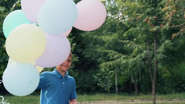 Child with balloons in his hands. Boy plays in the summer park. Spins around itself.