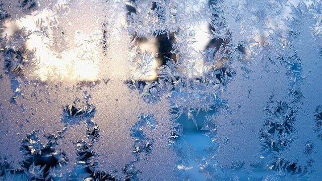 Window glass with frozen drops in the form of white snowflakes on a cold winter evening. Abstract natural Christmas frost background on blue