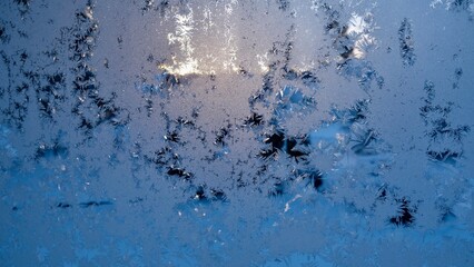 Window glass with frozen drops in the form of white snowflakes on a cold winter evening. Abstract natural Christmas frost background on blue