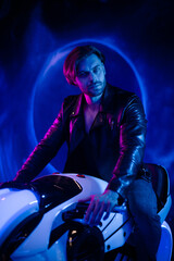 Fototapeta na wymiar A handsome cyberpunk man in the dark sits on a space motorcycle. A guy in a leather jacket in the scenery of the future in neon color flies through space.