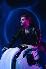 Fototapeta na wymiar A handsome cyberpunk man in the dark sits on a space motorcycle. A guy in a leather jacket in the scenery of the future in neon color flies through space.