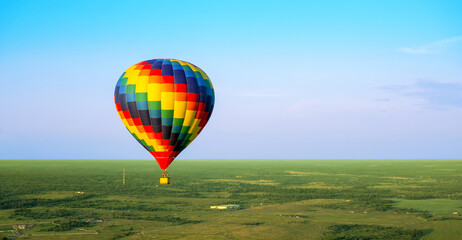 Obraz premium A colorful air balloon is flying in free flight over the field. Bird's-eye view. Multi colored balloon in the blue sky
