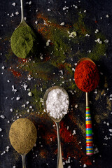 Old metal spoons with different kind of spices on black background