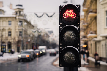 Bicycle traffic light with bicycle icon and active red resolving light on background of city in winter day