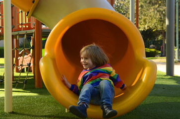 Cute boy in a colorful sweater on the playground. The child laughs, plays, rides down the slide....