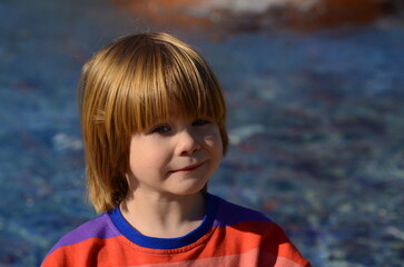 Positive little boy in sunglasses and a multi-colored jacket on the background of the water. Space...