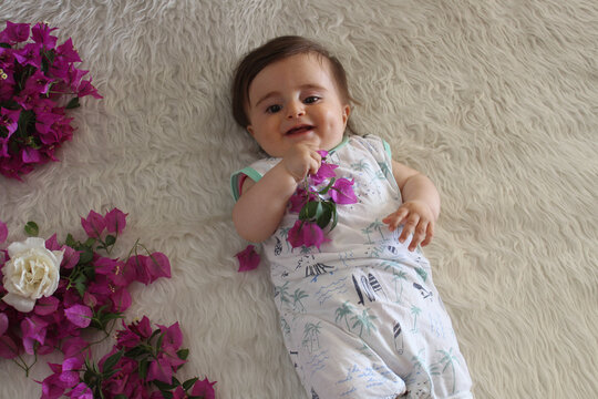 Cute baby play with begonvil flower and smiling on white fluffy blanket.