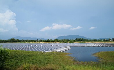 Side view of floating solar or floating photovoltaics, FPV, floatovoltaics on water surface in lake or reservoir, with beautiful view of grass field moutain and blue sky.