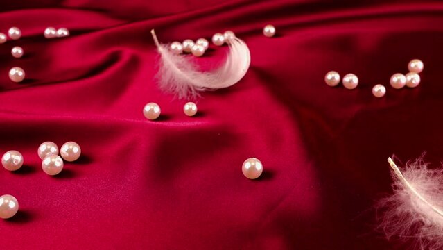 White swan feathers fall on red silk with pearls. Slow