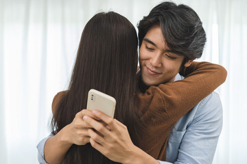 Cheating on girlfriends concept, unfaithful Asian man looking at mobile phone text during embracing...