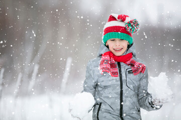 Naklejka na ściany i meble Portrait of a boy in a winter hat. Winter, outside, snow. A child plays with snow. Happy child in winter.