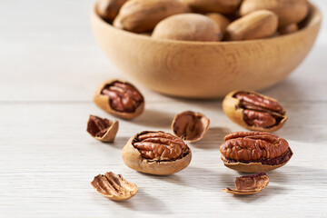 Pecan spill out of a wooden bowl on a white table, selective focus.