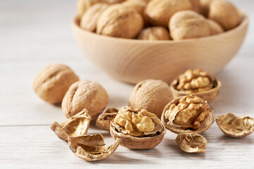 walnuts spill out of a wooden bowl on a white table, selective focus.