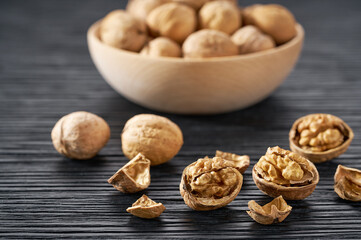 walnuts spill out of a wooden bowl on a black table, selective focus.