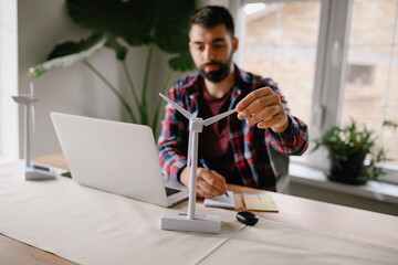 Young innovative dedicated bearded employee sitting in his modern office thinks about development of windmills. Sustainable development concept.
