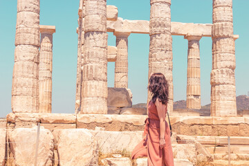A young girl in a brown summer dress looking at the ancient temple of Poseidon on the Cape Sounion, closeup