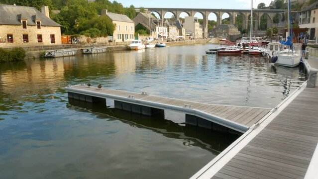The calm waters of the river named "Rance" in the medieval village of Dinan, Brittany, France. Several vessels and yachts at both sides. The famous bridge on the background with blue sky.