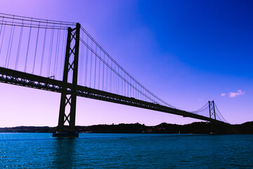 Silhouette of large metal bridge across the sea Strait on the background of a fantastic purple sky