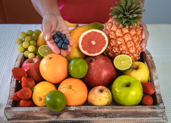 Close-up on a wooden basket full of colorful fresh fruit. Female hands holding some blueberries. Healthy nutrition and lifestyle concept.