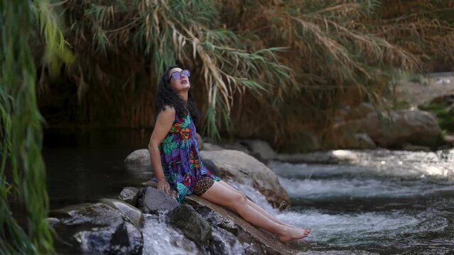 latin mid adult woman on a stone in the Elqui river enjoying the climate and nature of the Valle del Elqui, Cochiguaz