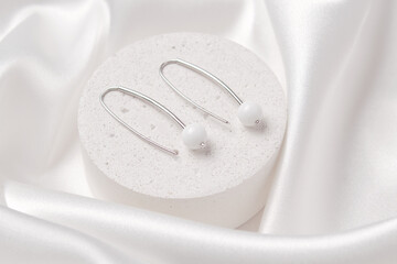 A product shot of two silver earrings with white agate on a concrete podium. Beautiful accessories...