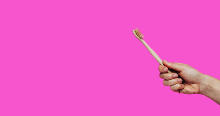 Wooden toothbrush in hand against pink background dental care concept.