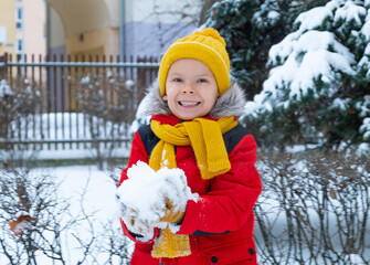 Cute little funny kid boy in colorful winter fashion clothes having fun and playing with snow,...