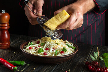 Professional chef adds hard cheese to the spaghetti plate. Working environment in the hotel kitchen. Delicious pasta with vegetables and spices