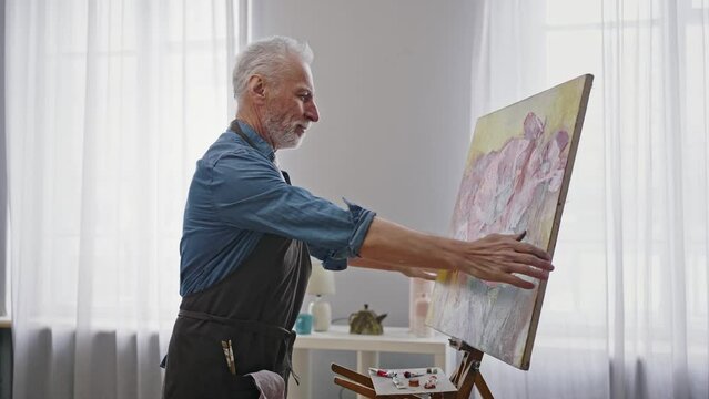 Caucasian elderly man at retirement, mature artist admires a finished canvas painting masterpiece