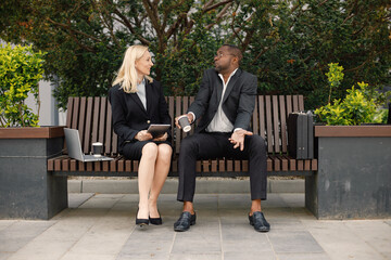 Black businessman sitting on a bench and talk with caucasian woman