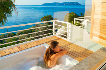 Young woman in yellow bikini relaxing in jacuzzi bath on hotel resort outdoors with beautiful view