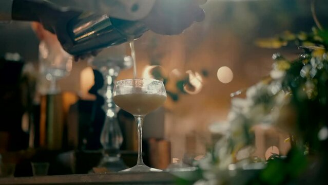 A bartender Shot from below of a bartender pouring a cocktail into a glass from a shaker at the bar. A bartender pours a cream-colored cocktail into a right glass from a shaker.