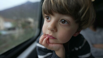 One contemplative small boy looking at landscape passing by inside train in motion. Portrait of a pensive child with hand in chin seated by window