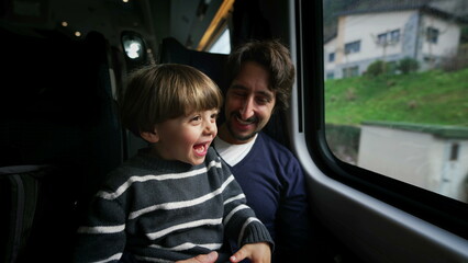 Happy father and son traveling together by train during vacation holidays. Little boy pointing with hand at landscape passing by inside transportation in motion
