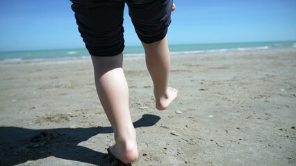 Child feet standing up at beach feeling the sand barefoot. Kid foot walking outside at ocean shore