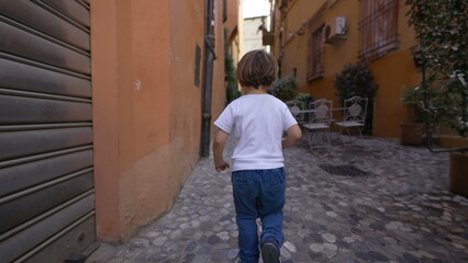 Obraz na płótnie Canvas Back of child running in old european street. One little boy runs in Italian alley