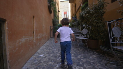 Fototapeta na wymiar Back of child running in old european street. One little boy runs in Italian alley