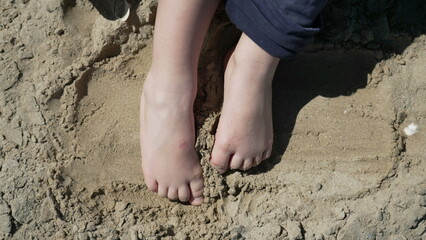 Child feet standing up at beach feeling the sand barefoot. Kid foot walking outside at ocean shore