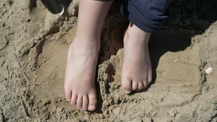 Child feet standing up at beach feeling the sand barefoot. Kid foot walking outside at ocean shore