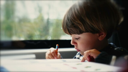 One concentrated kid doing kindergarten homework seated in train transportation. One little boy...