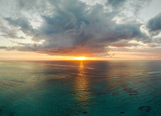 Sun is shining between the clouds and ocean at sunset time. The sunshine is reflecting in the water. ocean is beautiful clean blue color.