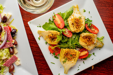 Grilled artichokes. Artichokes roasted in olive oil, topped with cheese sauce, garnished with scallions, parsley served in cast iron skillet. Classic American or French bistro side dish.