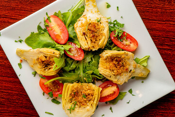 Grilled artichokes. Artichokes roasted in olive oil, topped with cheese sauce, garnished with scallions, parsley served in cast iron skillet. Classic American or French bistro side dish.