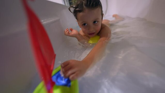 Child playing inside bathtub with toy boat. Playful small boy bathing inside tub