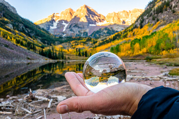 Maroon Bells lake at sunrise with hand glove holding glass crystal ball reflection in Aspen,...